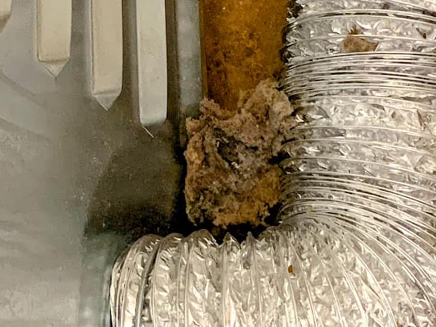 A flexible dryer duct crushed behind a machine with lint pushed out through the seams