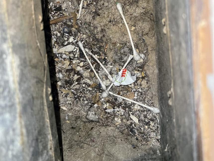 Debris and cotton swabs sitting in the bottom of a return duct under a bathroom floor