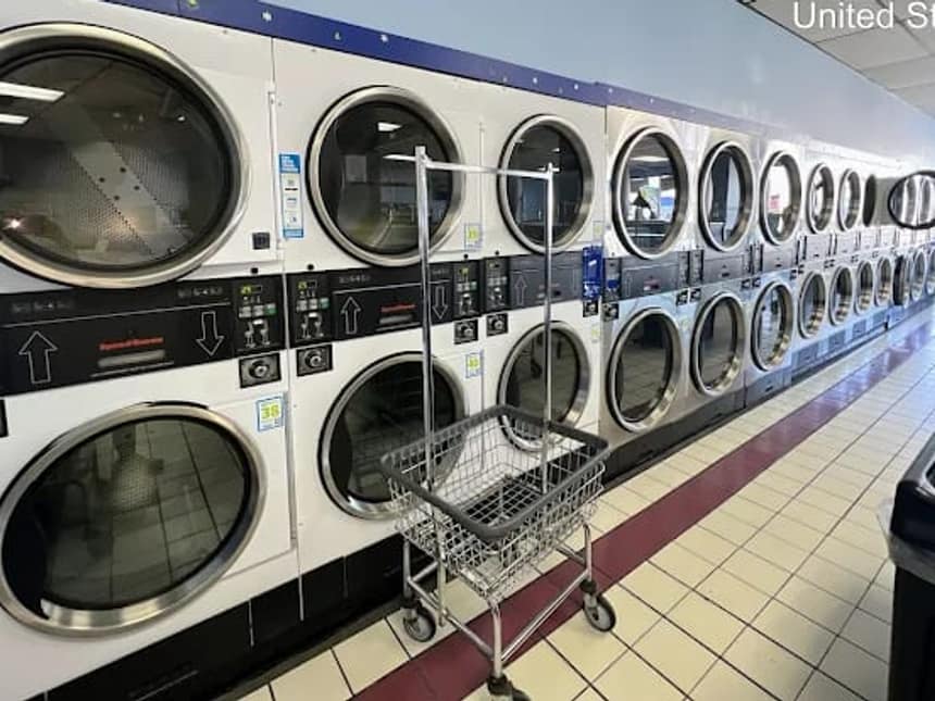 A long bank of commercial dryers in a Brookfield laundromat, every one of them venting to the same shared exhaust