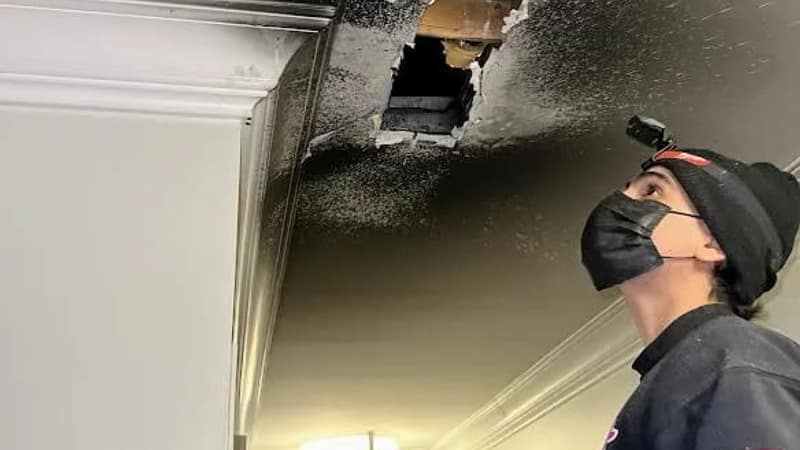 A Luxe Ducts technician in a respirator looking up at a smoke damaged ceiling burned open around the register