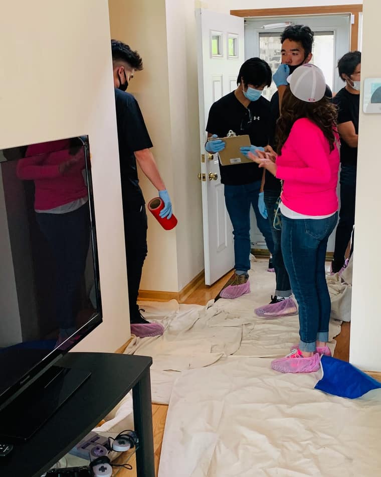 The Luxe Ducts crew in a client entryway in pink shoe covers, one technician writing up the walkthrough on a clipboard